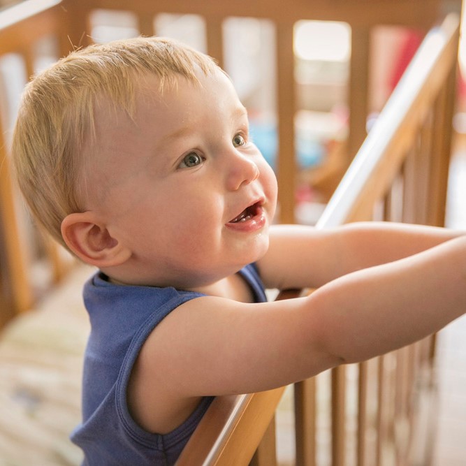 toddler boy in blue singlet reaching out of a timber cot